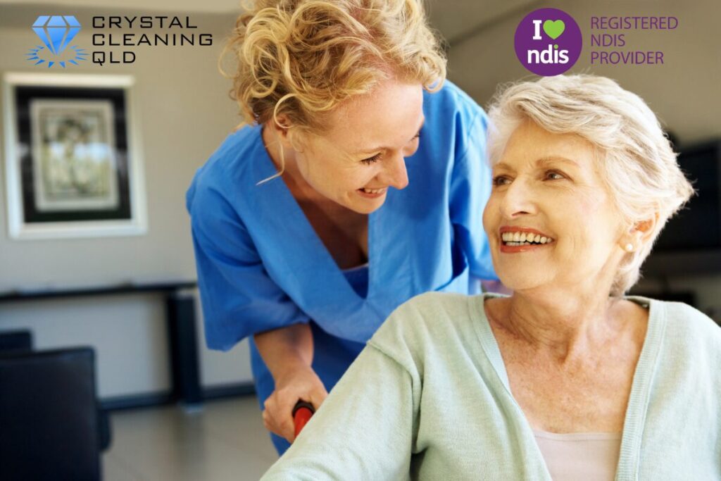 A friendly female support worker in a blue uniform smiling and communicating with a happy elderly woman in a wheelchair, showcasing how to improve cleaning and support services easily.
