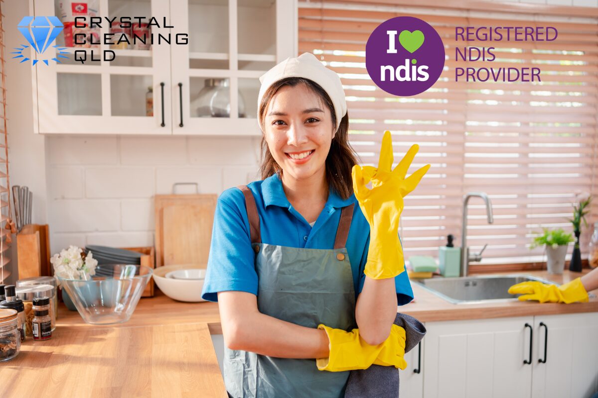 A smiling professional female cleaner in a bright kitchen giving an OK sign, representing NDIS Registered Provider Crystal Cleaning QLD in Brisbane and Gold Coast.