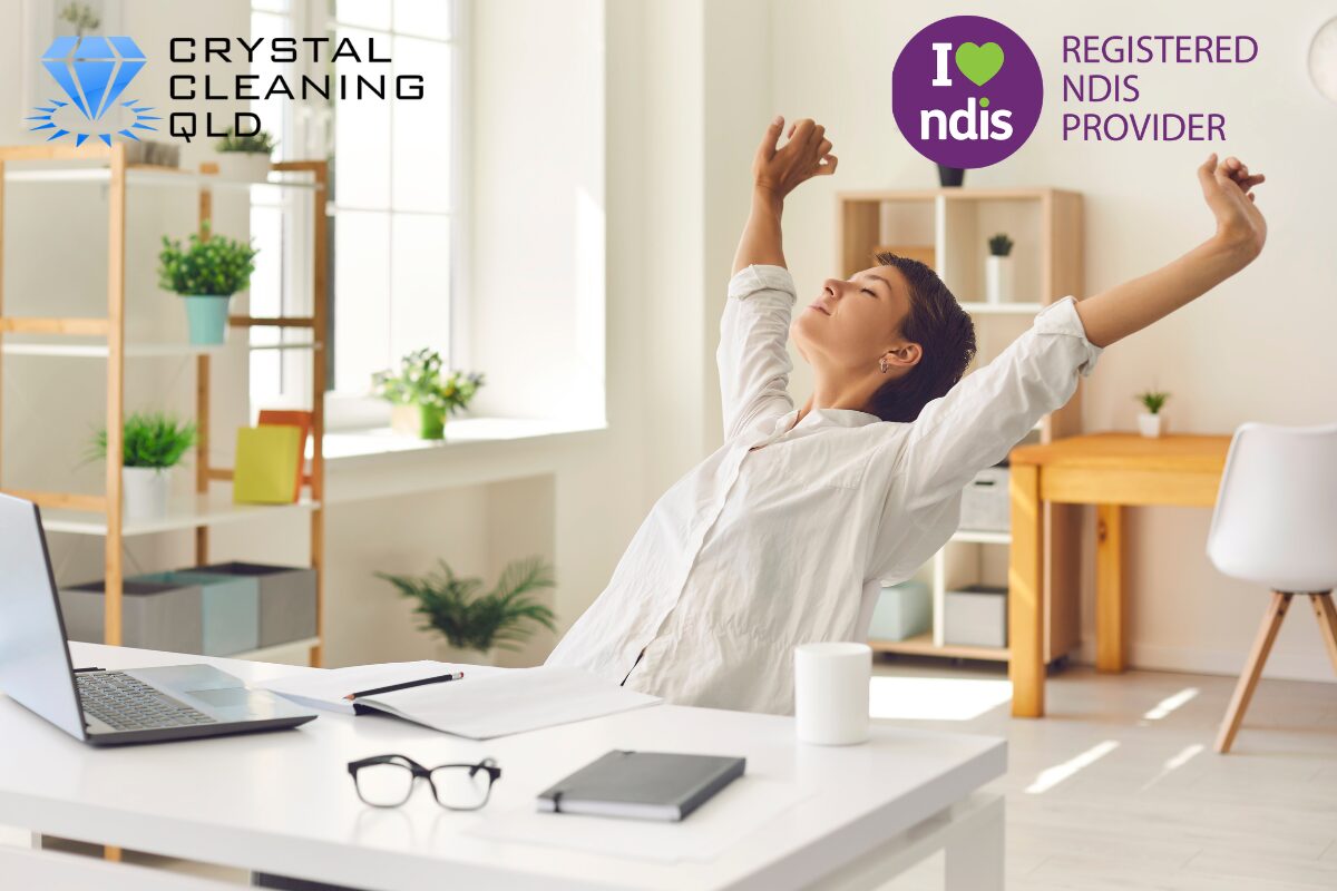 A relaxed woman stretching her arms at a clean desk in a bright room, showcasing a stress-free home environment supported by Crystal Cleaning QLD's NDIS domestic assistance services.